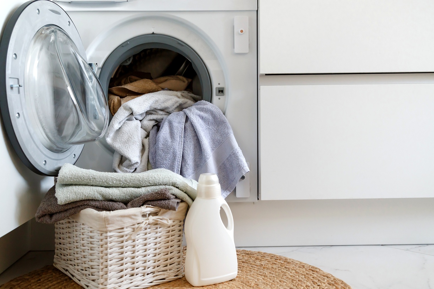 Loading a washing machine and washing clothes. A laundry basket and laundry gel in front of a household built-in washing machine in the kitchen.