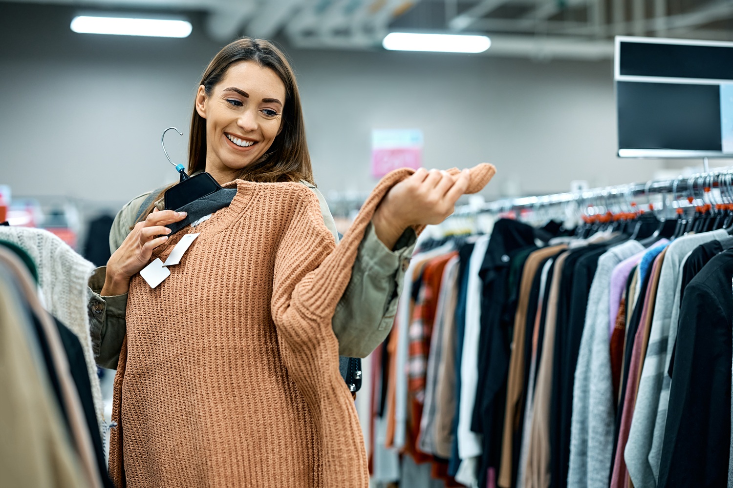 Happy woman trying on a sweater while shopping at clothing store.